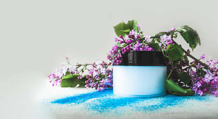 large blue jar with a moisturizing and cleansing cream for the skin and body with branches of purple lilac flowers and scattered with brilliant blue sequins. cosmetic bannerの写真素材
