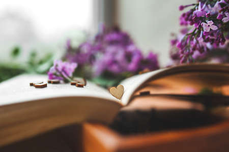 small wooden heart in an old open old yellow open book against a blurry bright bouquet of lilac lilac flowers. romanticheski Vitaminy the content, layout love, selective focusの写真素材