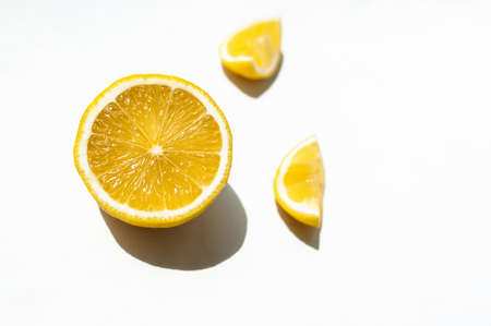 half a juicy ripe yellow lemon and two small slices on a white background with hard shadows in natural lightの写真素材
