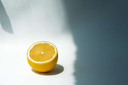 half a juicy ripe yellow lemon on a white background with hard shadows in natural lightの写真素材