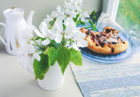 White porcelain cup with green tea and a fresh white pear tree flower and homemade berry pie with...