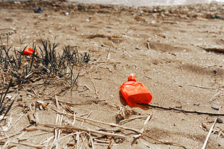Red Plastic trash on the sandy shore of the sea. The problem of ecological disaster and non-recyclable garbageの写真素材