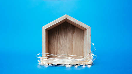 gray wooden small toy house wrapped garlands and lights on a clear bright blue backgroundの写真素材