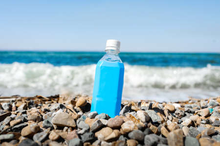 empty plastic blue bottle on a rocky beach against the background of a raging blue sea with waves...