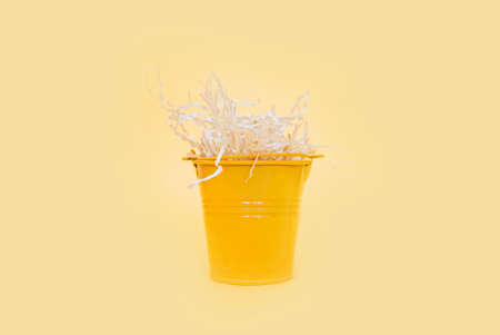 yellow metal miniature bucket filled with cut pressed paper on a clean yellow smooth backgroundの写真素材