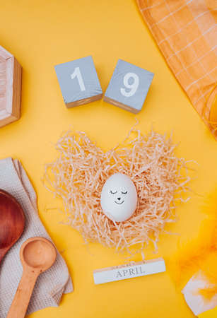 cute Easter egg with a black marker drawn face in a paper nest made of pressed paper, gray wooden...