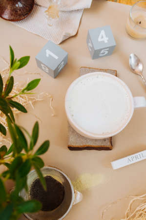 cozy home workplace for remote work during isolation and quarantine with a Cup of matcha with milk foam on a natural stone stand, a green home plant and a wooden perpetual calendar with the word aprilの写真素材