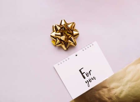 gold bow for decoration and notebook on a spiral with white sheets and black lettering for you on a delicate beige with gold foil backgroundの写真素材