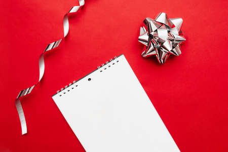 notebook on a spiral with white sheets on red background with a silver foil bow and silver curly ribbonsの写真素材