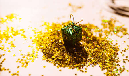 small green foil gift in the hard shadows against a background of scattered gold stars on a soft...