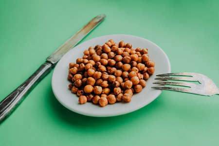 White farvor plate with fried ready-made chickpeas with spices, old worn silver spoon and fork on a...