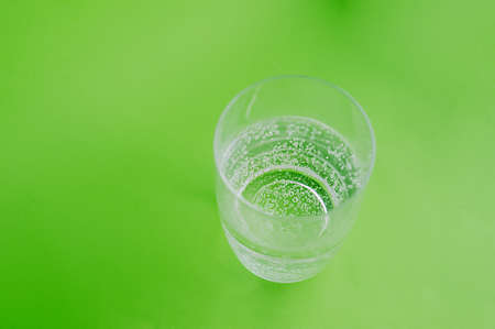 picture about a healthy lifestyle. Clear glass water glass full of pure carbonated water with bubbles on a clear green background. Top viewの写真素材