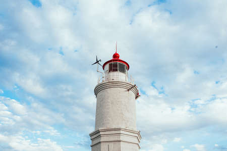 A white sea shore lighthouse with a red roof against a clear blue sky with white clouds on a Sunny day.の写真素材