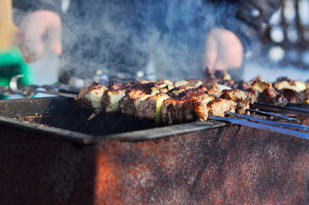 Cooking meat kebabs on fire and coals in the fresh air. Large puffs of smoke from cooking outside.の写真素材