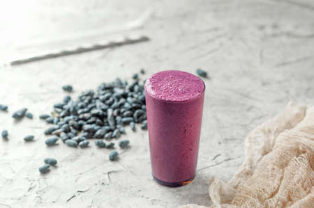 healthy vegetarian food, purple smoothies in a long glass mug on a light background and scattered...