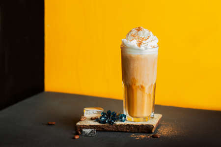 cold black coffee with whipped milk foam and spices in high glass on stand of natural stone, coffee...