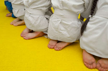 naked legs and heels of children in white tracksuits with wrestling belts on a yellow mattressの写真素材