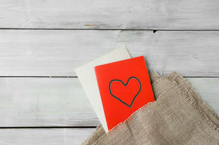 red paper card with heart and white envelope on rough cloth on light wooden table. holiday image for loversの写真素材
