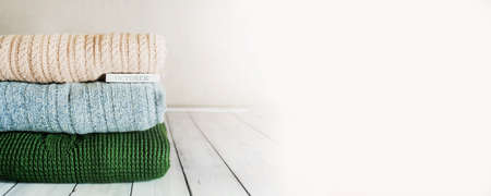 cozy autumn banner stack of warm knitted sweaters in pastel colors and the inscription October on a light wooden table in the roomの写真素材