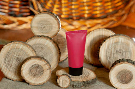red cosmetic cream tube surrounded by wooden round pieces of different sizes, trendy cosmetic layout