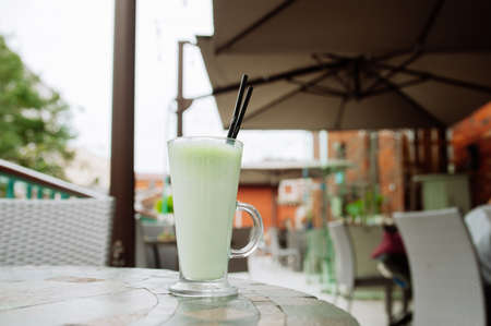 Cup of matcha tea with tubes on the table of the restaurant terraceの写真素材