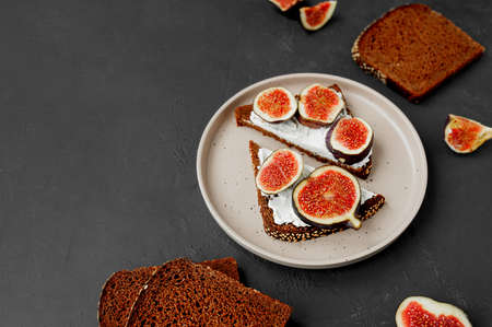triangular sandwiches with figs, cream cheese on black bread with seeds on flat porcelain plate, black table with ingredients, top view, selective focusの写真素材