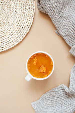 vertical image of delicious soup with breadcrumbs in white mug, knitted beige sweater and wicker...