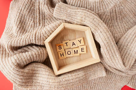 stay at home, lettering in wooden square letters in small wooden house on knitted beige sweater. Monochrome picture, warning for the period of the second wave of coronavirusの写真素材