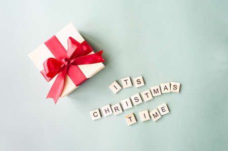 its Christmas time, lettering in wooden square letters on mint-colored background and festive gift box with red satin ribbon. Minimalism holiday greetings, selective focusの写真素材