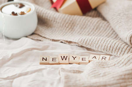 new year inscription on beige crumpled fabric, gift box with red ribbon, garlands on beige knitted sweater on background. festive cozy new year card, selective focusの写真素材