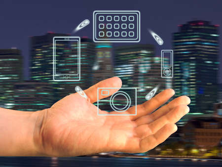 Various devices over a palm against a panorama of a night sityの写真素材
