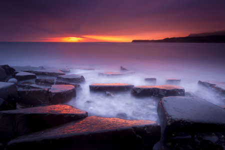 The sun sets on the beautiful Dorset coastline illuminating glistening rocks with orange and yellow highlightsの写真素材