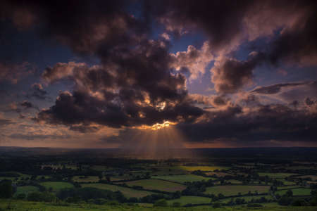 Golden sunlight beams through holes in clouds over the Blackmore Vale