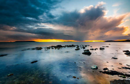 Rain-bearing clouds hang over the horizon casting reflections in the still waters off the Dorset coastlineの写真素材