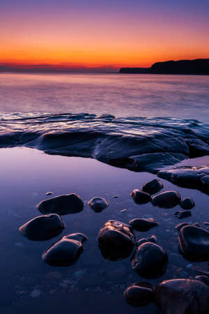 The sun sets on the beautiful Dorset coastline illuminating glistening rocks with orange and yellow highlightsの写真素材