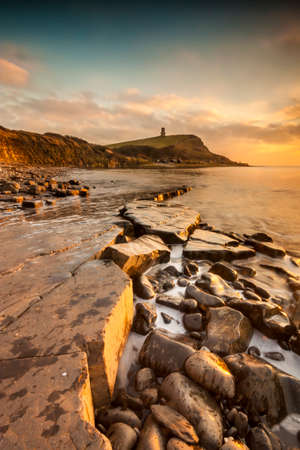 The sun sets on the beautiful Dorset coastline illuminating glistening rocks with orange and yellow highlightsの写真素材