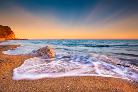 The sun sets illuminating the wet rocks and pebble beaches of the Jurassic Coastの写真素材