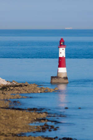 Red and white lighthouse on still, blue waters situated at the bottom of white, chalk cliffs