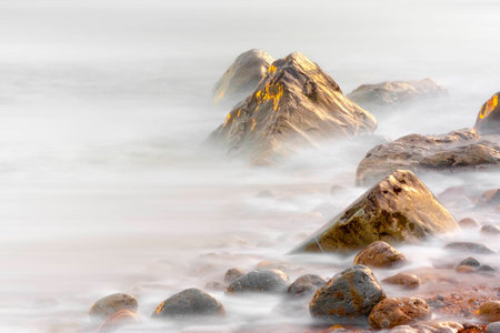 The beach at Osmington at sunset with breaking waves on the shoreline using very slow speed causing the scene to look like misty mountainsの写真素材