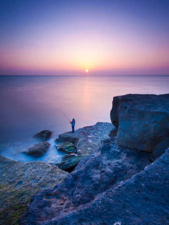 As the sun goes down over Portland Bill the sea calms and washes gently against the rocksの写真素材