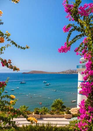 Clear blue waters and beautiful flowers can be seen past the Lighthouse at Ortakent in Turkeyの写真素材