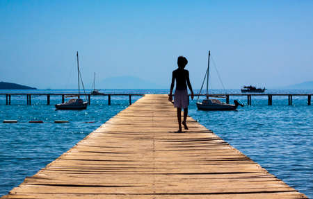 A boy admires boats as he walks out towards the seaの写真素材