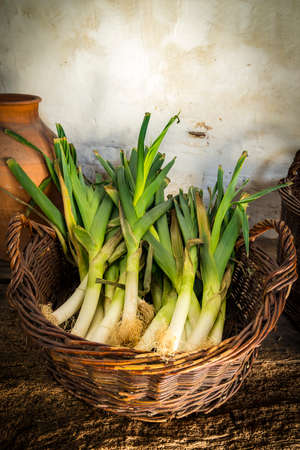 Green leeks arranged in a wicker basket on a rough wooden tableの写真素材