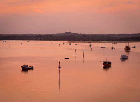 Orange skies over a Dorset harbour with various boats silhouetted on the seaの写真素材