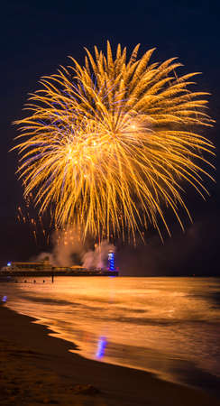 Multi colored Fireworks in the dark blue sky reflected on the wet sand and in the sea at Bournemouth...