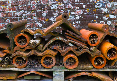 Insect hotel made with recycled wood, terracotta flower pots and roof tiles, found in a country house garden against a brick wall.の写真素材