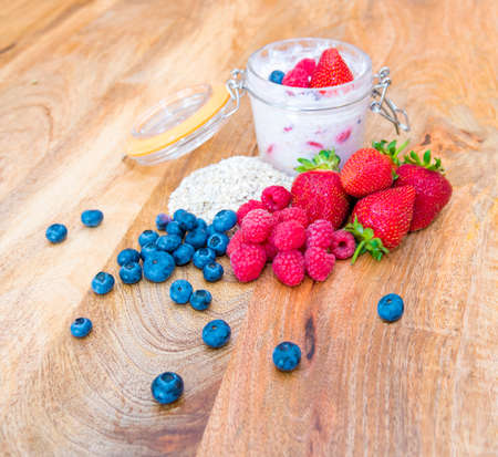 Glass jar of Healthy breakfast - overnight oats - fresh strawberries, raspberries and blueberries sitting on a mango wood tableの写真素材