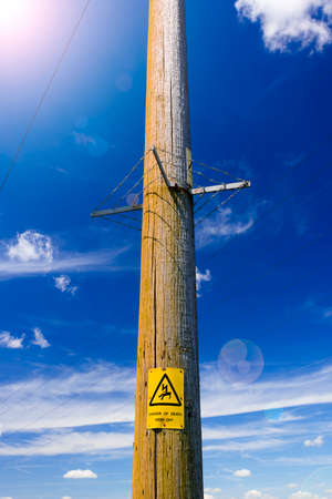 Electricity poles reach up into the deep blue sky. A warning sign warns of impending dangerの写真素材