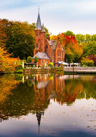 Fairytale buildings cast reflections in the Minnewater Canal in Bruges, Belgium on a still autumn dayの写真素材