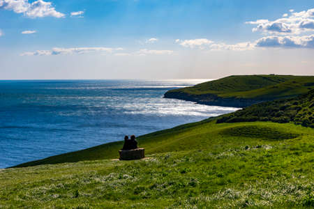 Steep, grassy, green hills along the Dorset coast above Dancing Ledge with ramblers taking a rest...